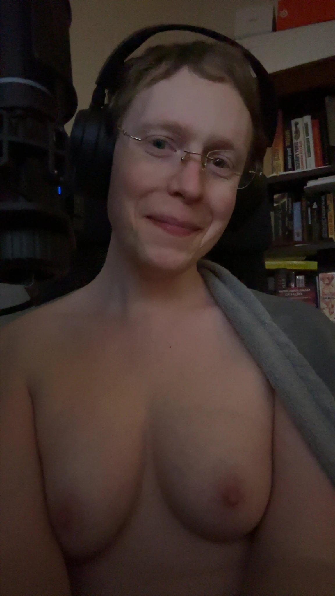Siina smiling at the camera with her grey blanket mostly fallen off her, exposing her breasts.