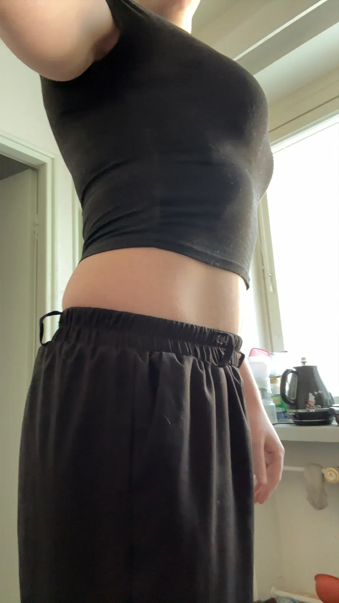 Side picture of Siina in a black crop top and black pants, showing off her abdomen and curves.